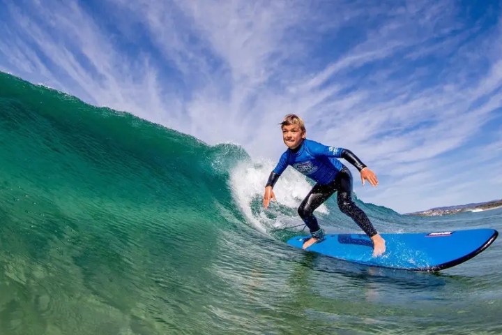 Person surfing a green wave on a blue board, under a clear blue sky.